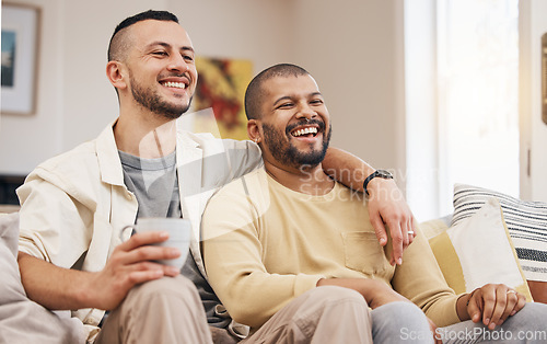 Image of Happy, laugh and gay couple watching a movie on a sofa while relaxing with a cup of coffee. Love, bonding and young lgbtq men with a latte streaming a film, show or video online in the living room.