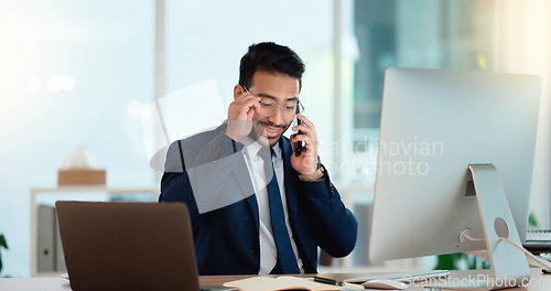 Image of Happy business man talking on his phone while working on a computer and smiling alone at work. Young corporate professional having a discussion and explaining project details to a colleague or client