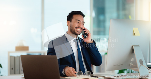 Image of Happy business man talking on his phone while working on a computer and smiling alone at work. Young corporate professional having a discussion and explaining project details to a colleague or client