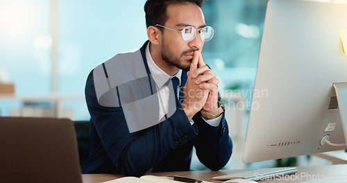 Image of Thinking IT manager working on a desktop computer and laptop in a modern office. Information Technology software engineer analyzing data management system. Thoughtful analyst looking for a solution