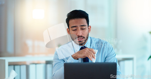Image of A modern business man feeling sick with covid fatigue while working online at a desk on his laptop. Closeup of an male corporate manager blowing his nose. An ill office worker frustrated at work.