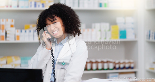 Image of Friendly pharmacist talking on the telephone and checking something on her computer in a pharmacy. Woman using pc to access drug database for inventory check or access customers prescription online