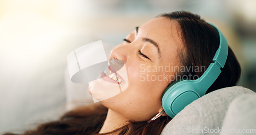 Image of Relax, headphones and happy woman listening to music, radio or podcast while resting on sofa. Happiness, smile and calm girl from singapore sitting on the couch in living room at home with technology