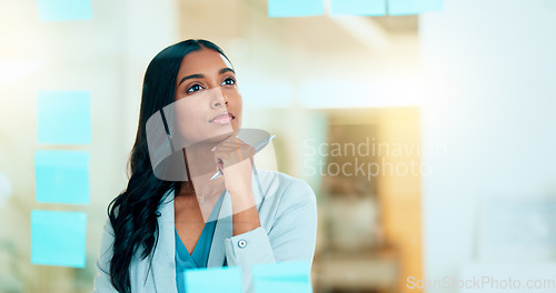 Image of Serious business woman brainstorm project ideas at a board with colorful sticky notes. Female marketing manager standing and writing business plan. Office worker thinking about corporate strategy.