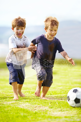 Image of Having a friendly game. Two cute little boys playing soccer together outside while covered in mud.