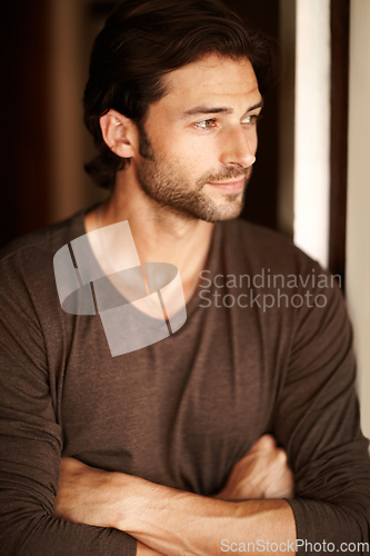 Image of Content with his lot in life. A handsome young man gazing out of a window with his arms folded.