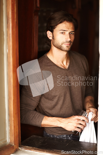 Image of Long night ahead. Shot of a handsome young man drying off a glass while looking through a window.