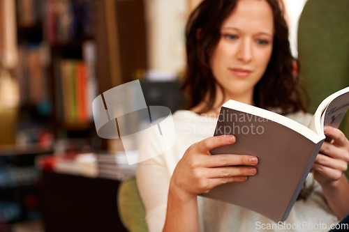 Image of Immersed in the words. A young woman quietly reading a book while seated in a chair.