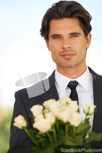 Image of A peace offering. Portrait of a handsome young man wearing a suit and holding a bunch of roses.