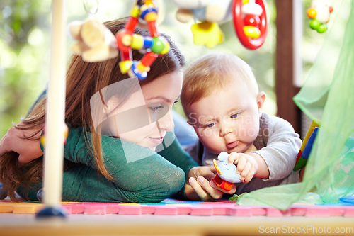 Image of Filled with curiousity. Cute young mom lying alongside her infant son on the playroom floor.