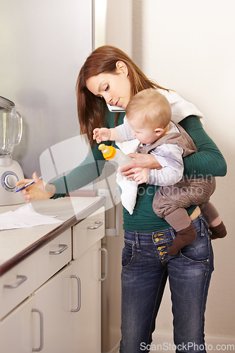 Image of Being a mom is a real juggling act. Young mom trying to multi-task while holding her baby son and his bottle.