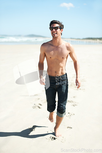 Image of Fun in the sun. An attractive young man walking on the beach.