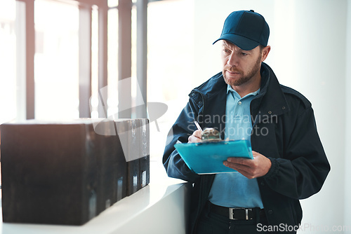 Image of Making sure every delivery is signed and dated. Shot of a handsome delivery man writing on his clipboard while waiting in the lobby with a customers order.