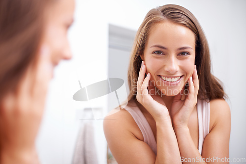 Image of Shes the fairest of them all. A young woma touching her face happily as she looks in the mirror.