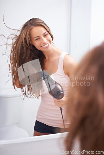 Image of Taking care of her luscious mane. A young woman blow drying her hair in front of a mirror.