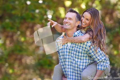 Image of Look over there. A handsome man giving his wife a piggyback outdoors.