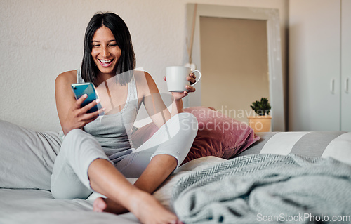 Image of Mornings are for coffee and social media. Shot of a young woman using a smartphone and enjoying a cup of coffee in bed at home.