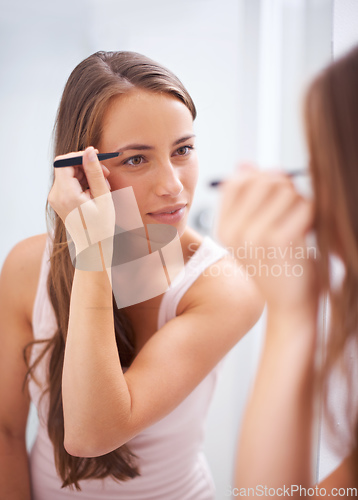 Image of Creating the perfect arch. A young woman tweezing her eyebrows in front of a mirror.