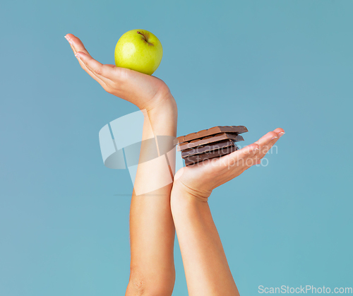 Image of The healthy choice is in your hands. Cropped studio shot of a woman holding up chocolate and an apple against a blue background.