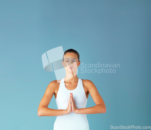 Image of Namste my healthiest me. Studio shot of a fit young woman meditating against a blue background.