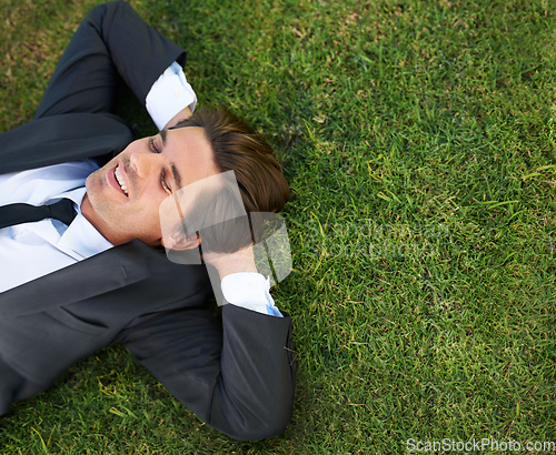 Image of Just taking a breather. A young businessman lying down on green grass.