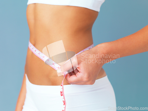 Image of The proof is in the inches. Cropped studio shot of a fit young woman measuring her waist against a blue background.