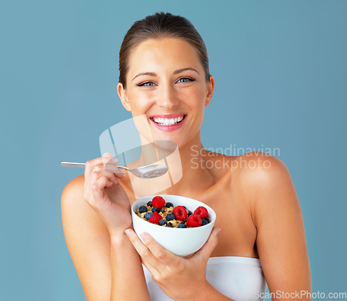 Image of Healthiness and happiness go hand in hand. Studio shot of an attractive young woman eating a bowl of muesli and fruit against a blue background.