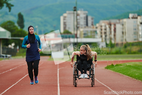 Image of A Muslim woman in a burqa running together with a woman in a wheelchair on the marathon course, preparing for future competitions.