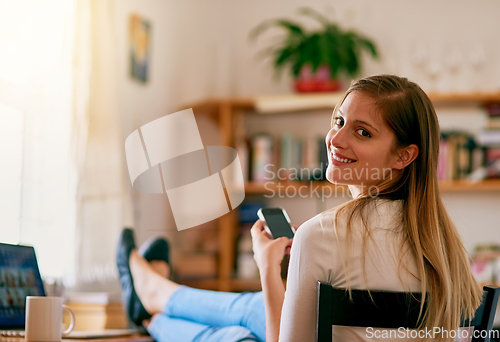 Image of I cant imagine my life without wifi. Portrait of a young woman using her smartphone while sitting at her desk at home.