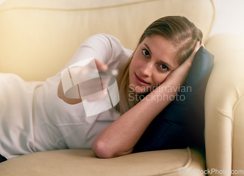 Image of Settling in for a soap opera marathon. Portrait of a young woman using a remote to change the channels on her TV at home.