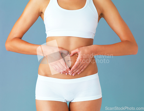 Image of For the greatest wealth, invest in your health. Cropped studio shot of a fit young woman making a heart shaped gesture over her stomach against a blue background.