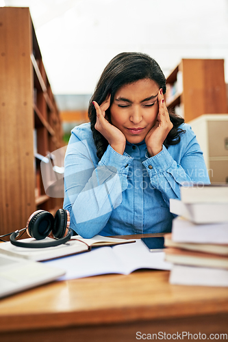 Image of I wont let this headache stop me from my studies. Shot of a university student looking stressed out while working in the library at campus.