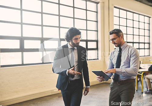 Image of Wireless technology keeps their business moving forward. Shot of two well-dressed businessmen brainstorming together over a tablet in their office.