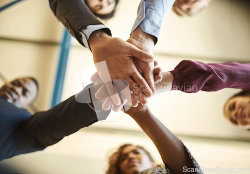 Image of Brought together by business. Low angle shot of a team of businesspeople piling their hands on top of each other in the office.