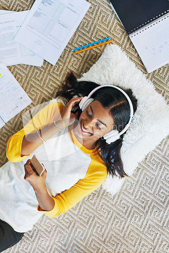 Image of Selecting the perfect music to study to. High angle shot of a young female student listening to music while studying at home.