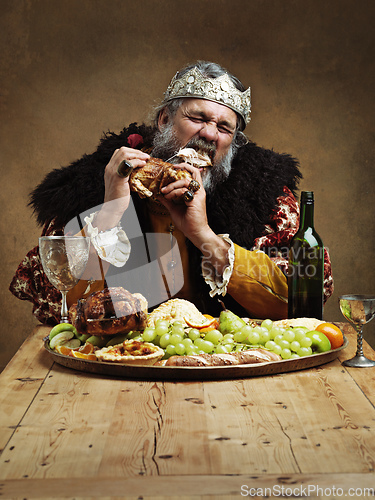 Image of Ruling is hungry business. A mature king feasting alone in a banquet hall.