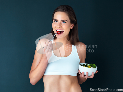 Image of Theres always room for healthy food. Studio portrait of an attractive young woman eating a salad against a dark background.