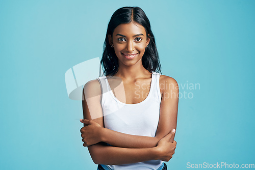 Image of Confident and content. Studio portrait of a beautiful young woman standing with her arms crossed against a blue background.