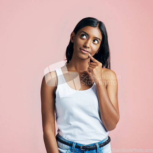 Image of Let me think about that.... Studio portrait of a beautiful young woman looking thoughtful against a pink background.