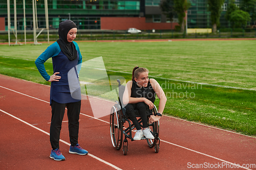 Image of A Muslim woman wearing a burqa resting with a woman with disability after a hard training session on the marathon course