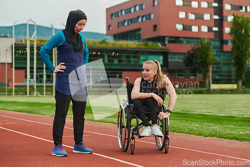 Image of A Muslim woman wearing a burqa resting with a woman with disability after a hard training session on the marathon course