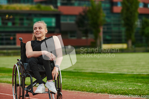 Image of A smiling woman with disablitiy sitting in a wheelchair and resting on the marathon track after training