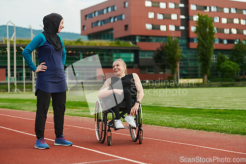 Image of A Muslim woman wearing a burqa resting with a woman with disability after a hard training session on the marathon course