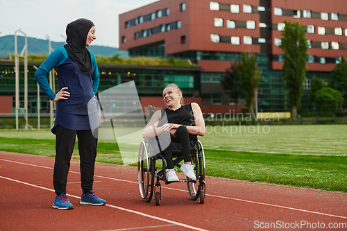 Image of A Muslim woman wearing a burqa resting with a woman with disability after a hard training session on the marathon course