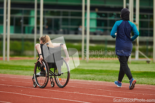 Image of A Muslim woman in a burqa running together with a woman in a wheelchair on the marathon course, preparing for future competitions.