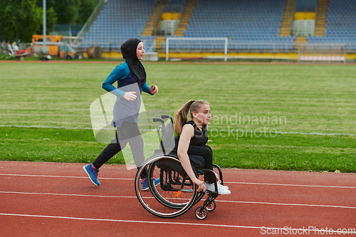 Image of A Muslim woman in a burqa running together with a woman in a wheelchair on the marathon course, preparing for future competitions.