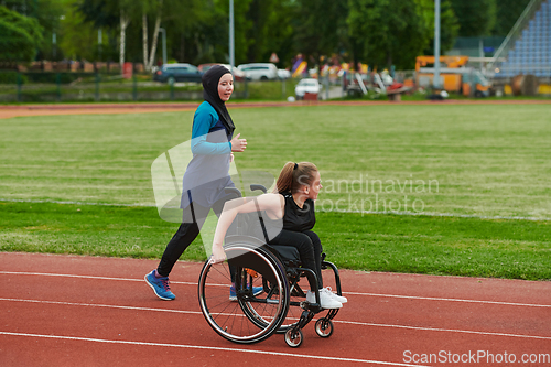 Image of A Muslim woman in a burqa running together with a woman in a wheelchair on the marathon course, preparing for future competitions.