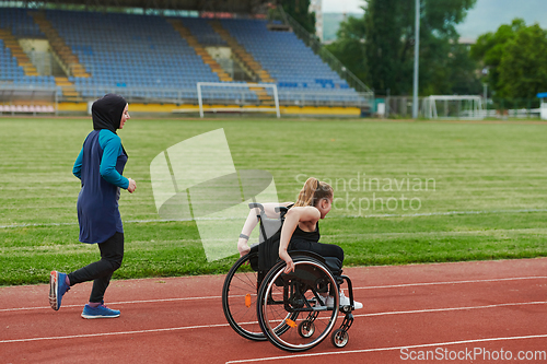 Image of A Muslim woman in a burqa running together with a woman in a wheelchair on the marathon course, preparing for future competitions.