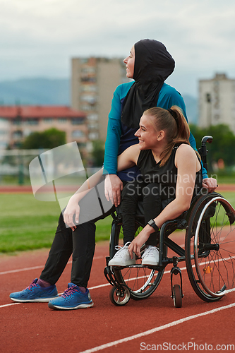 Image of A Muslim woman wearing a burqa resting with a woman with disability after a hard training session on the marathon course