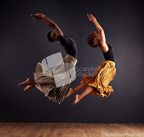 Image of Synchronisity. Two contemporary dancers performing a synchronized leap in front of a dark background.